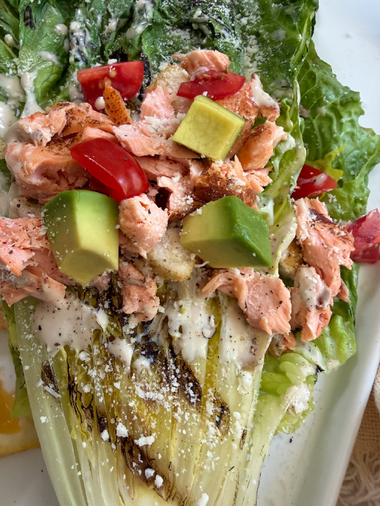 Grilled Salmon Caesar Salad served with charred romaine lettuce, California King Salmon, croutons, avocado, and creamy Caesar dressing.
