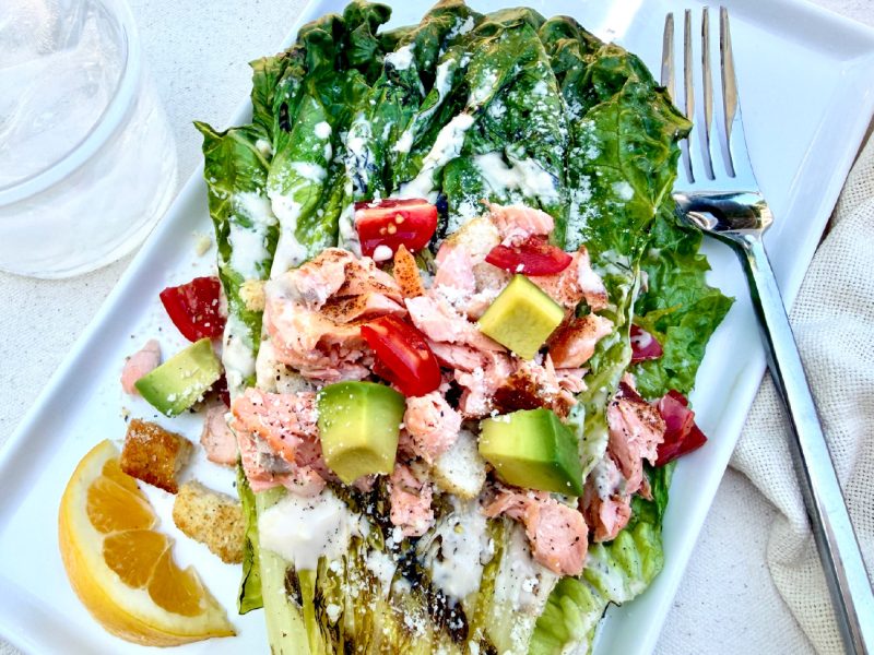 Grilled Salmon Caesar Salad with charred romaine, avocado, tomatoes, Parmesan cheese, croutons, and California King Salmon.