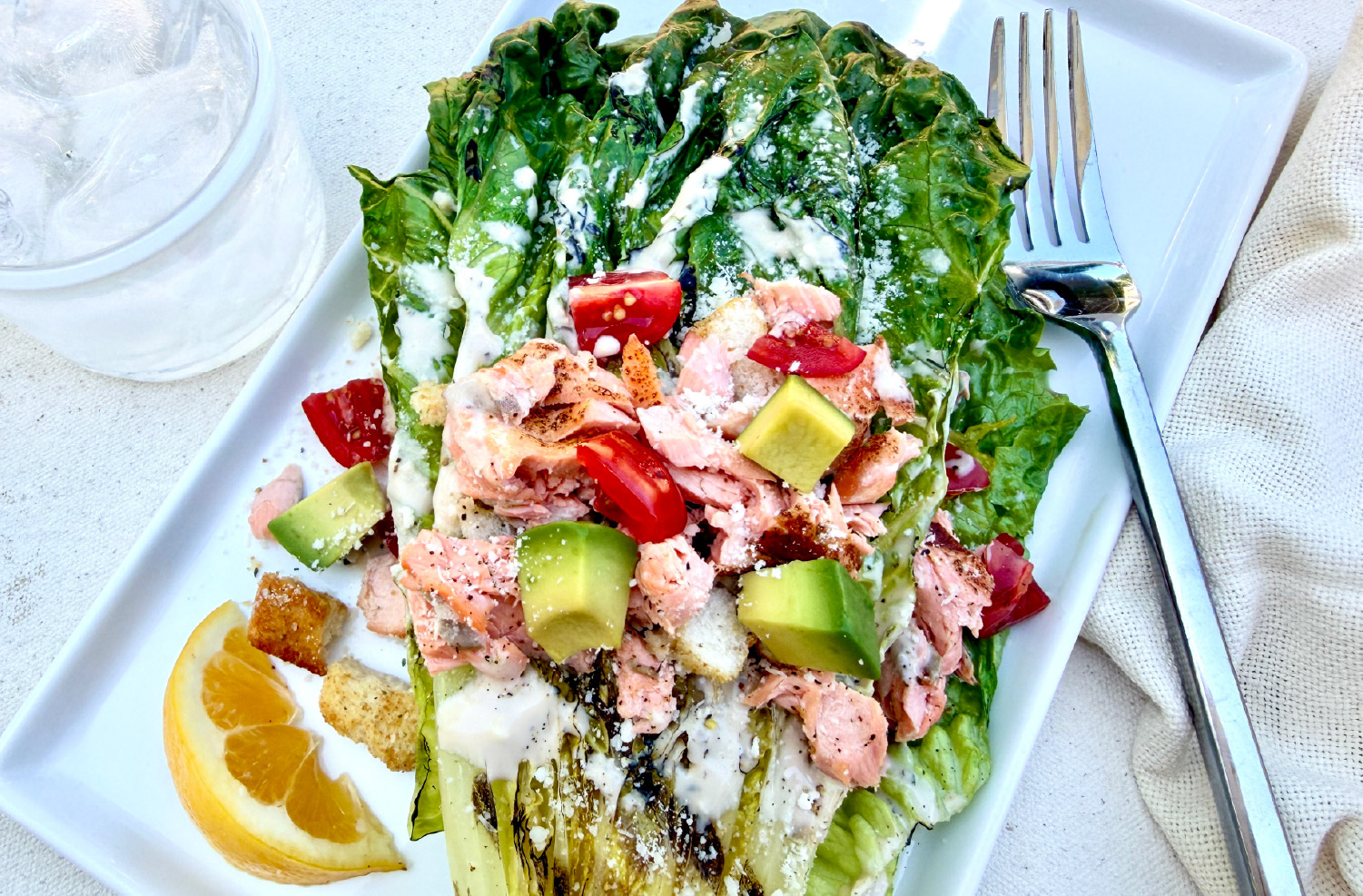 Grilled Salmon Caesar Salad with charred romaine, avocado, tomatoes, Parmesan cheese, croutons, and California King Salmon.